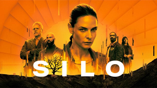 An orange-toned poster for "Silo," featuring a woman with dark hair in the foreground. Behind her are four additional characters, each with serious expressions. The background includes radial lines and a barren tree, with the title "SILO" prominently displayed at the bottom, premiering at Comic-Con on July 27.