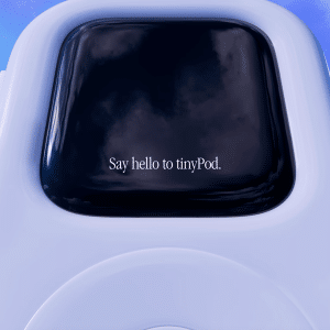 Close-up view of the new product, a small white device with a screen displaying "Say hello to tinyPod." The background features a blue sky with pink streaks, giving a modern, technological impression. It’s like the Apple Watch, but even more compact and innovative.