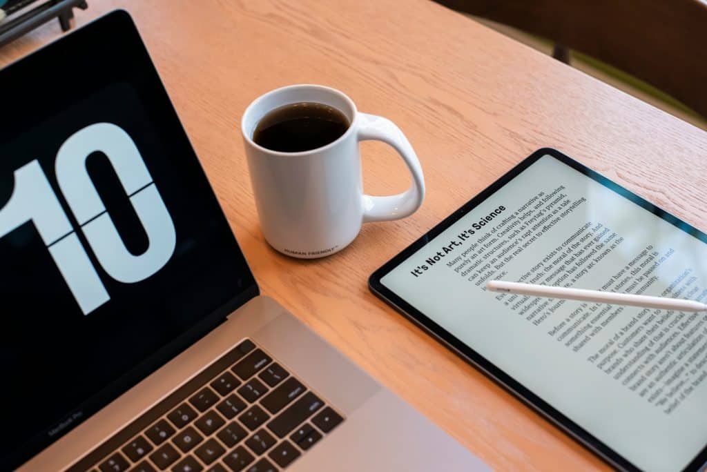 A workspace with a Mac displaying the number '10,' a white mug filled with coffee, and a tablet showing text titled "It's Not Art, It's Science." There is also a stylus resting on the tablet. The surface is a light wooden table, perfect for diving into PDF Editors or following a Comprehensive Guide.