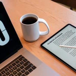 A workspace with a Mac displaying the number '10,' a white mug filled with coffee, and a tablet showing text titled "It's Not Art, It's Science." There is also a stylus resting on the tablet. The surface is a light wooden table, perfect for diving into PDF Editors or following a Comprehensive Guide.