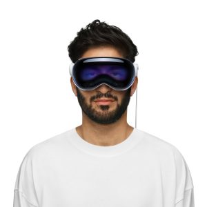 A man with dark hair and a beard wears a white shirt and an Apple Vision Pro headset. The sleek device covers his eyes and part of his face with its reflective dark screen, creating an immersive experience. The background is plain white, hinting at the UK launch's minimalist style.