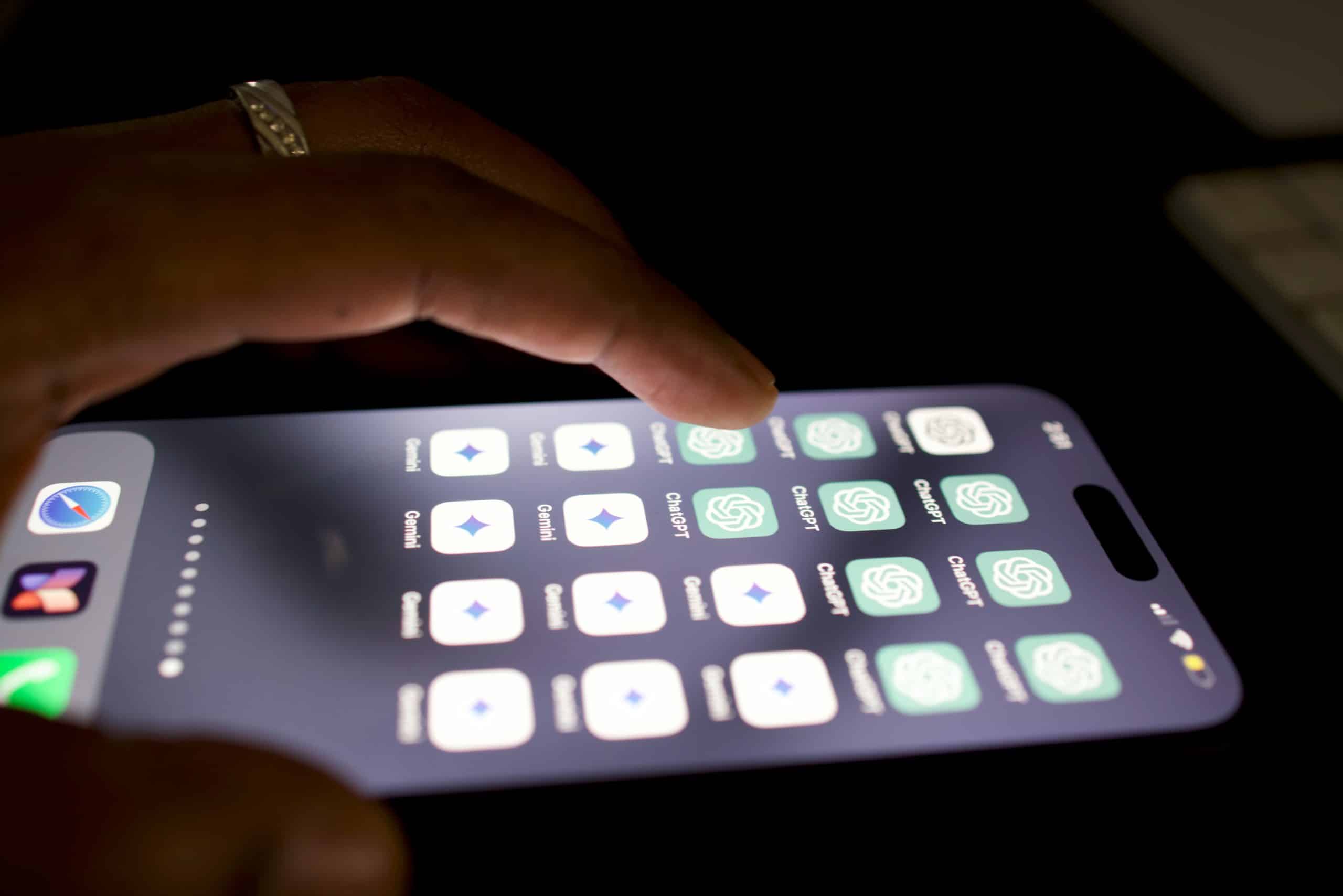 A close-up of a hand holding a smartphone, with a finger touching the screen. The screen displays several rows of app icons, most of which appear to be identical and feature a green and white design resembling a chat or messaging app logo. Among them is an icon for SearchGPT, an AI-powered search engine. The background is dark.