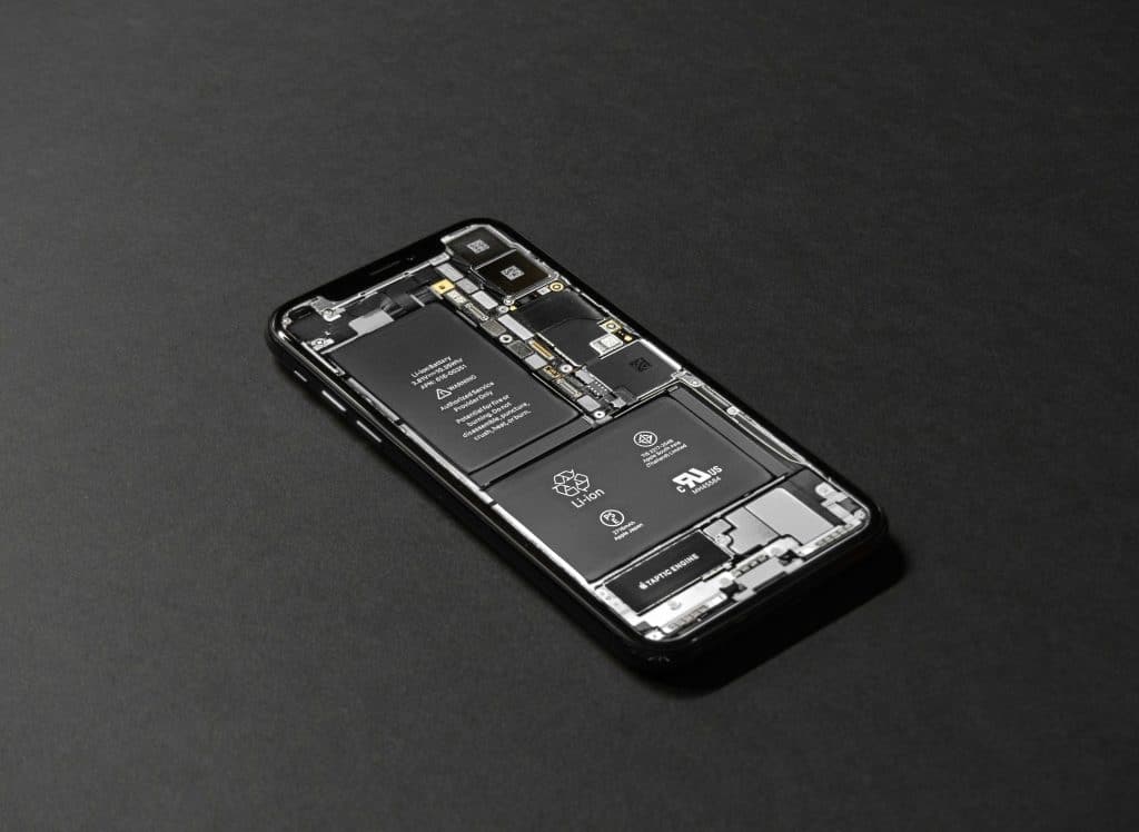 A smartphone is displayed on a dark surface with its back cover removed, exposing the internal components such as the battery, circuits, and various hardware parts. The detailed view highlights the intricate design and arrangement of the internal elements seen in 2025 iPhones.