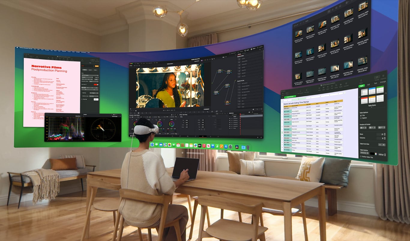 A person sitting at a wooden table in a modern living room wears an augmented reality headset, displaying multiple large virtual screens with various applications, ranging from video editing and color grading to project planning and gaming on iPhones, floating in front of them.