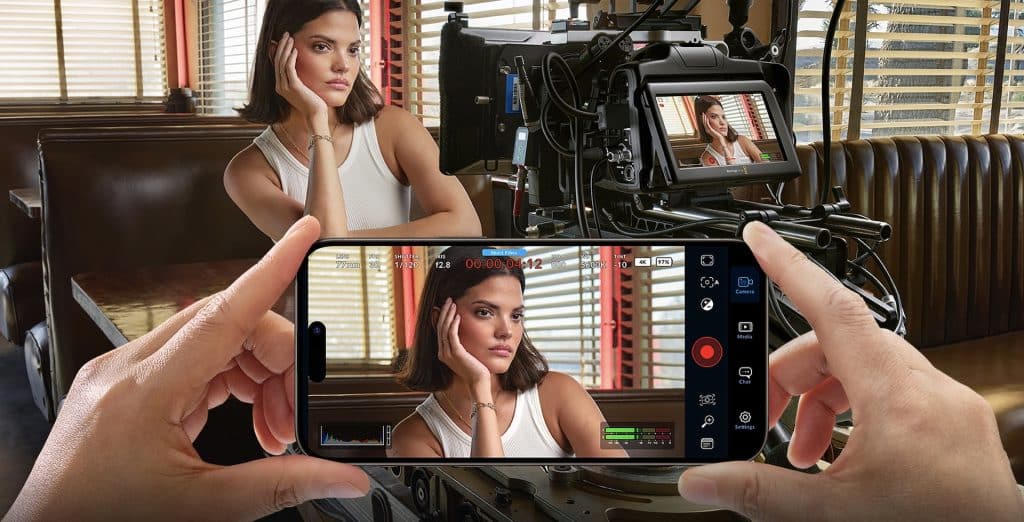 A woman sits with her chin resting on one hand, looking contemplative, in a diner booth. The scene, captured using the Blackmagic Camera App, is monitored on an iPad version, which mirrors the live view from the camera perfectly.