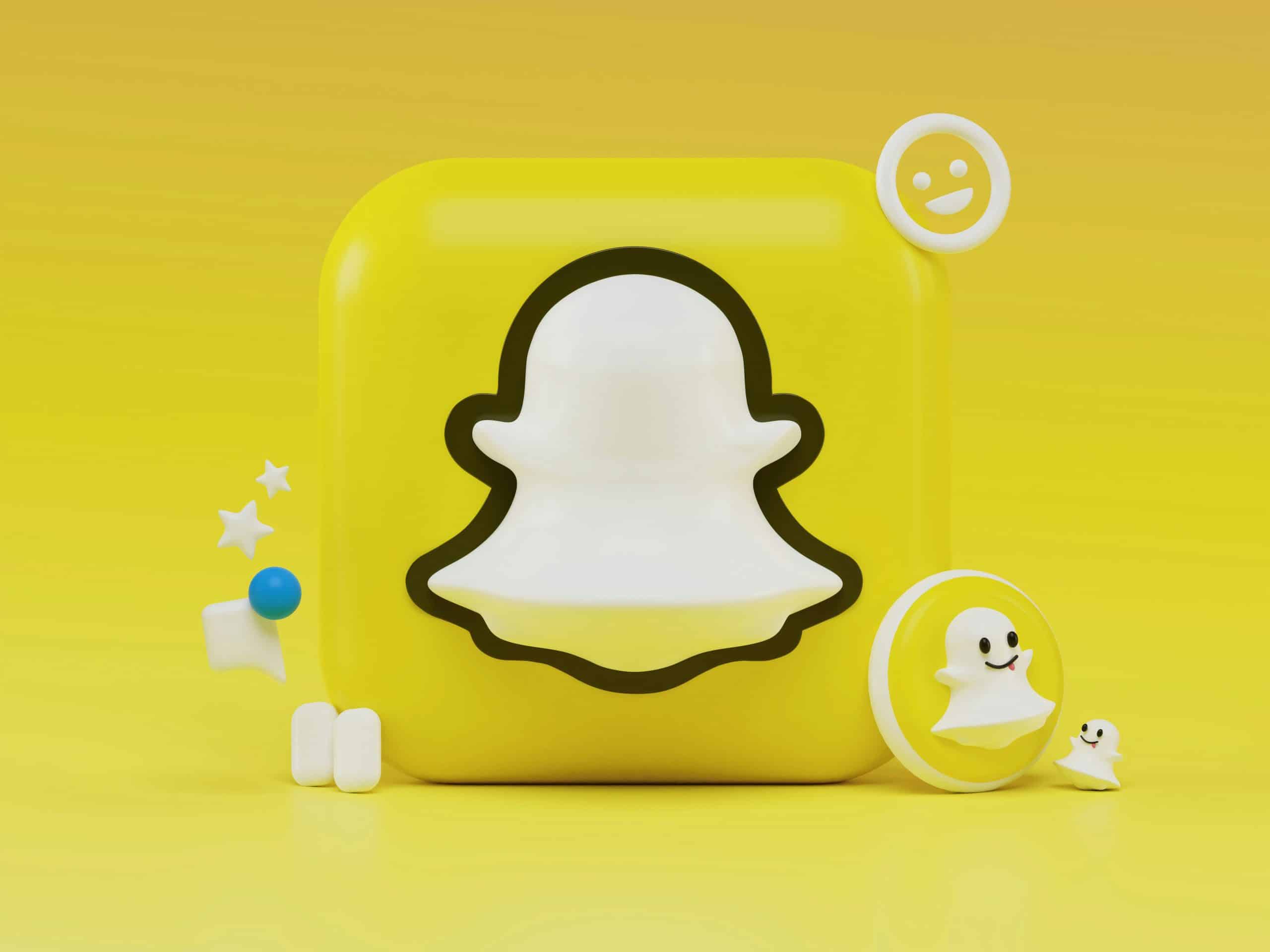 A 3D rendering of the Snapchat logo. The image features a white ghost outline on a yellow square background with various related 3D elements, including stars, emojis, and speech bubbles, surrounding the logo. The entire scene captures the playful and engaging spirit of Snapchat.