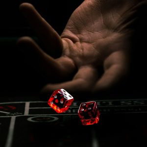 A hand is captured in mid-motion, about to release two red dice onto a casino table. The background is dark, highlighting the illuminated dice and creating a dramatic atmosphere reminiscent of top entertainment apps.