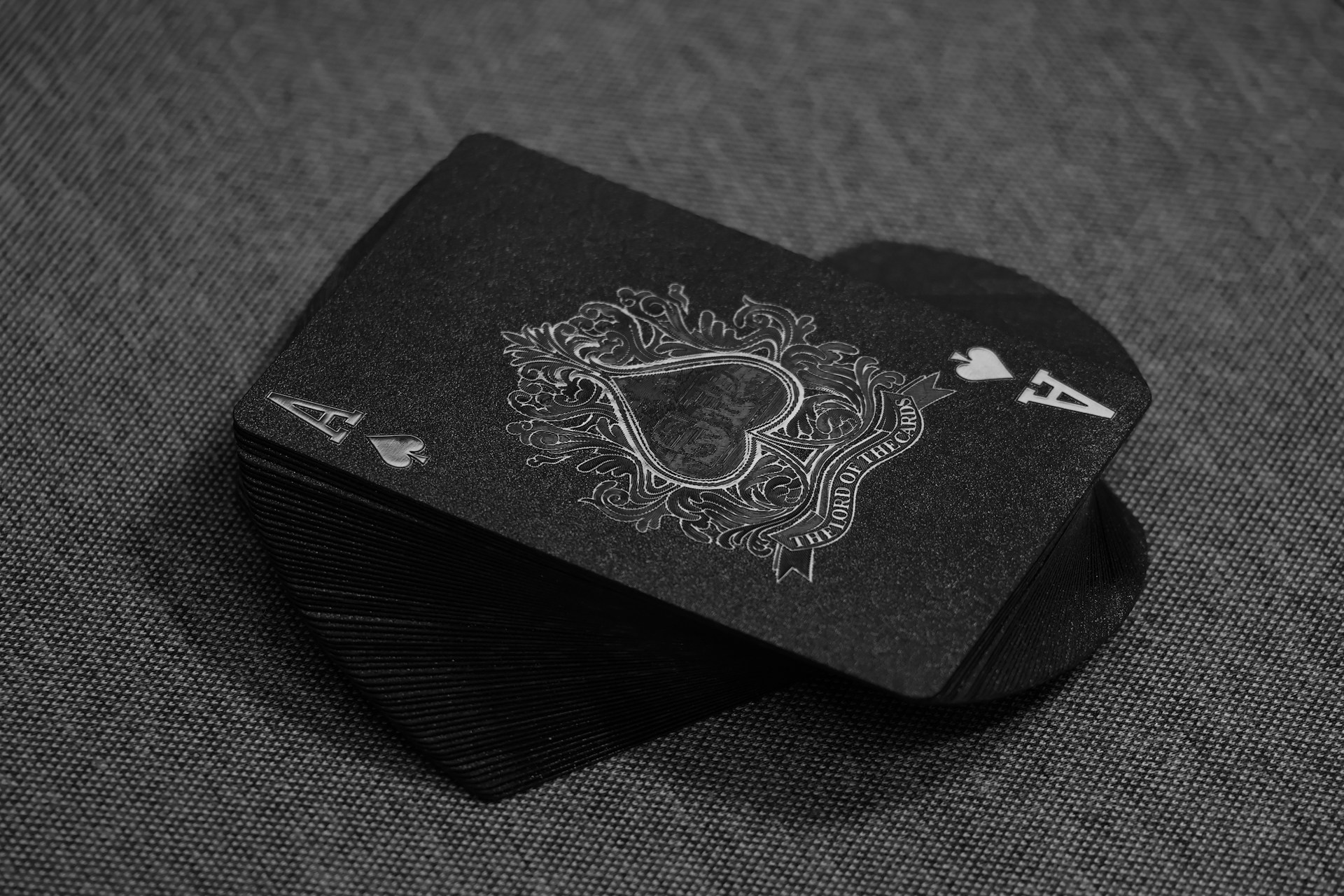 A stack of black playing cards sits on a textured surface, the top card being the Ace of Spades. It features intricate white detailing and an ornate design around the spade symbol, making it perfect for improving strategy, much like top iOS apps designed to sharpen your skills.