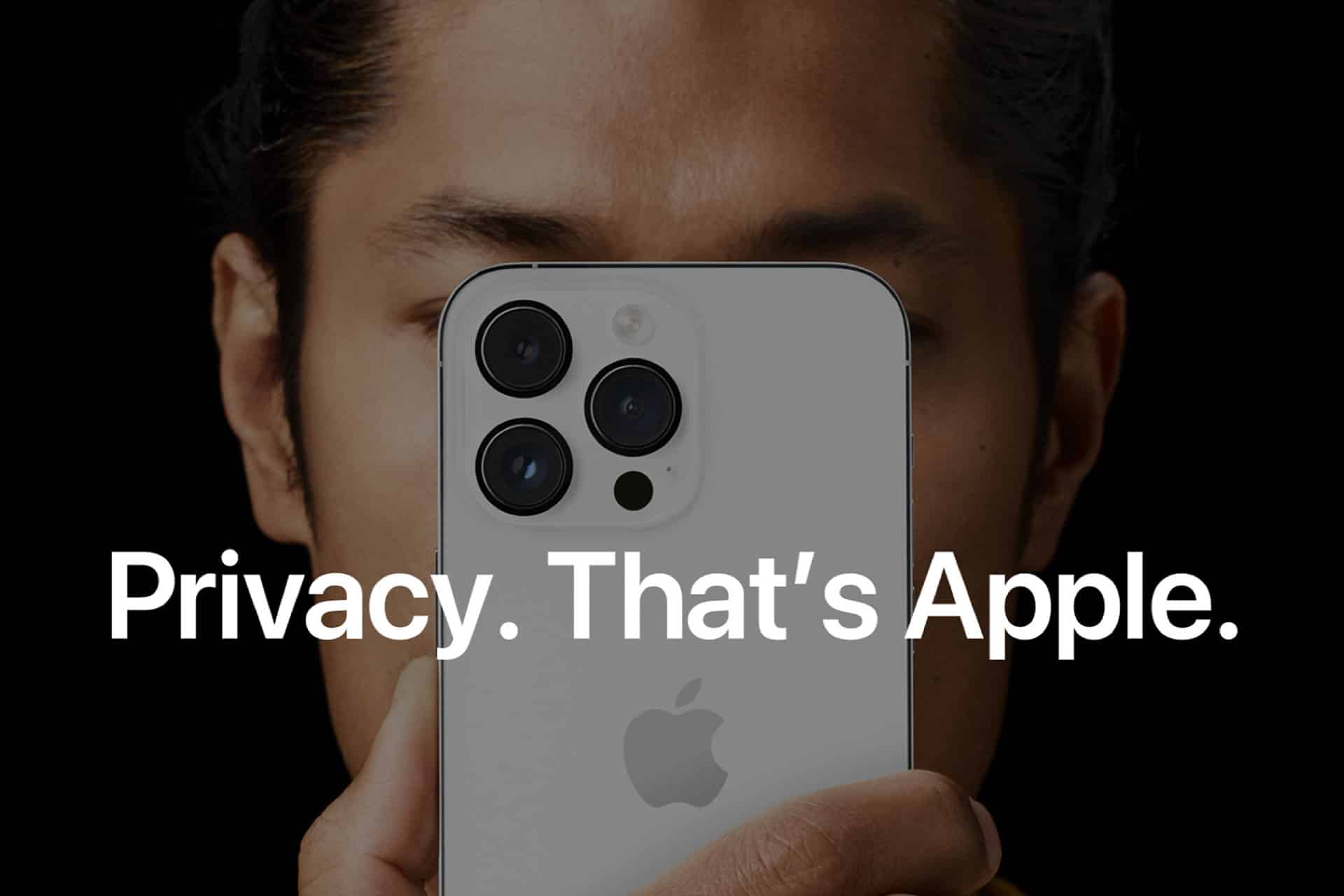 A person is holding an iPhone close to their face, with the back of the phone and its cameras prominently visible. The text on the image reads, "Privacy. That's Apple." The background is dark, emphasizing the phone and the text.