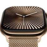 Apple Watch Series 10: A close-up of an Apple Watch Series 10 with a gold stainless steel case and a matching gold mesh band. The watch face displays an intricate, radial, golden pattern with white hour and minute hands. The AppleMagazine logo is visible in the bottom right corner.