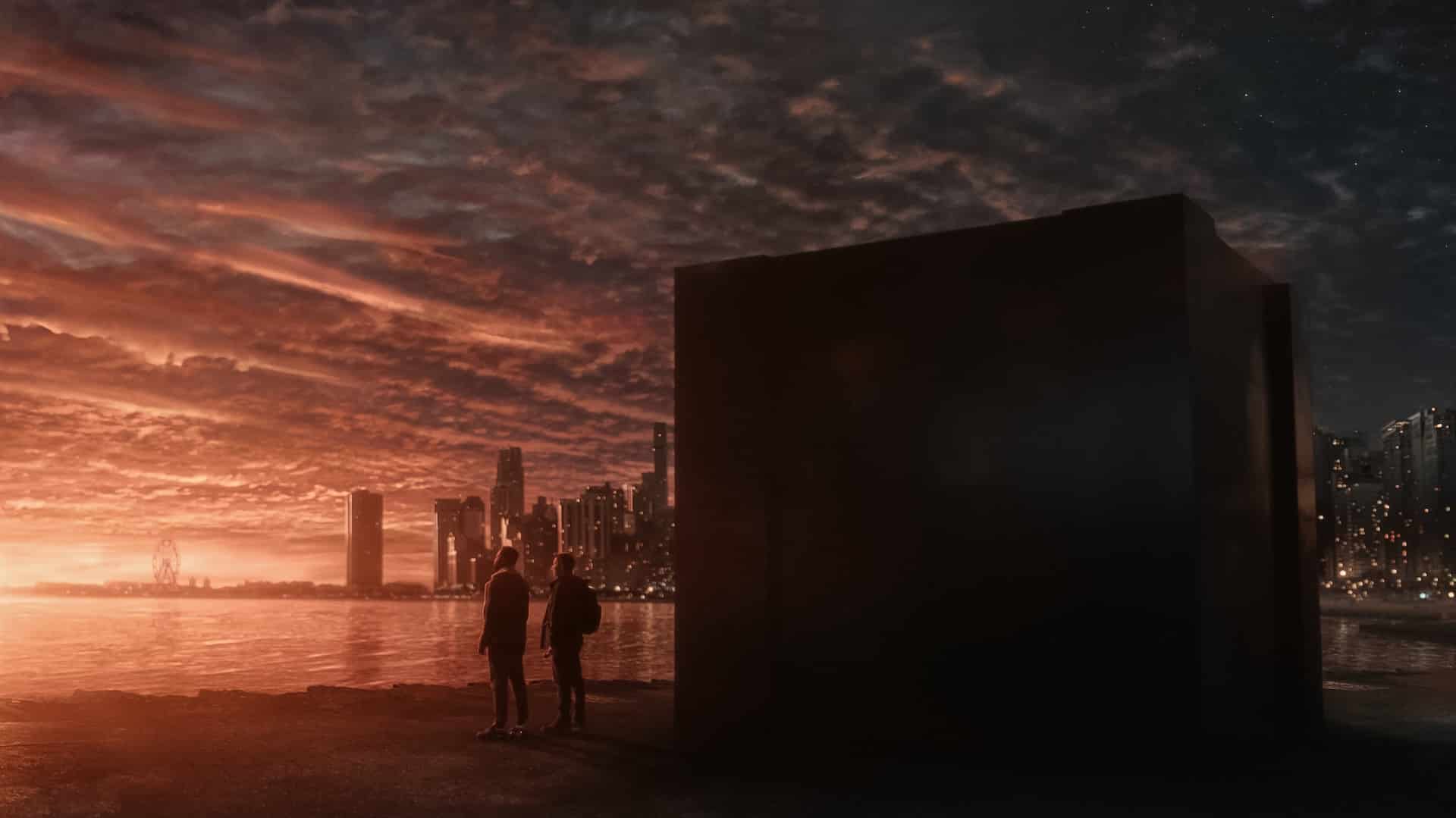 Dark Matter Series Season 1 | Apple TV+ | Two silhouetted figures stand by a massive, dark cube at a waterfront as the sun sets. A city skyline with illuminated buildings and a Ferris wheel is visible in the background under a dramatic, cloud-filled sky—an evocative scene reminiscent of Dark Matter Season 2.