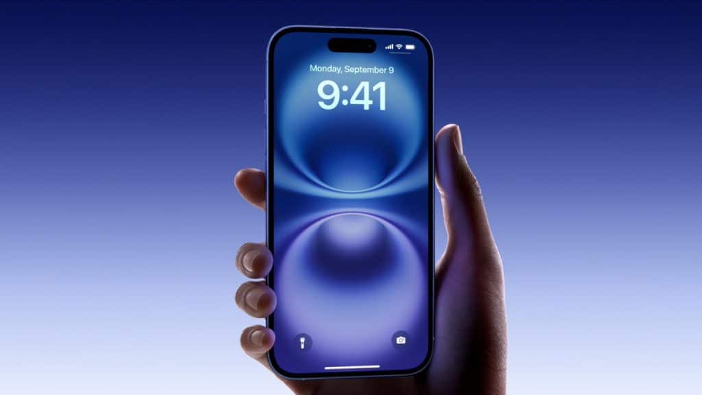 A hand holding an iPhone 16 with a blue, futuristic wallpaper displayed on the screen. The time shown is 9:41 and the date is Monday, September 9. The background is a gradient of blue shades. Announced with thin bezels and a sleek design, it's everything you need to know about the latest model.