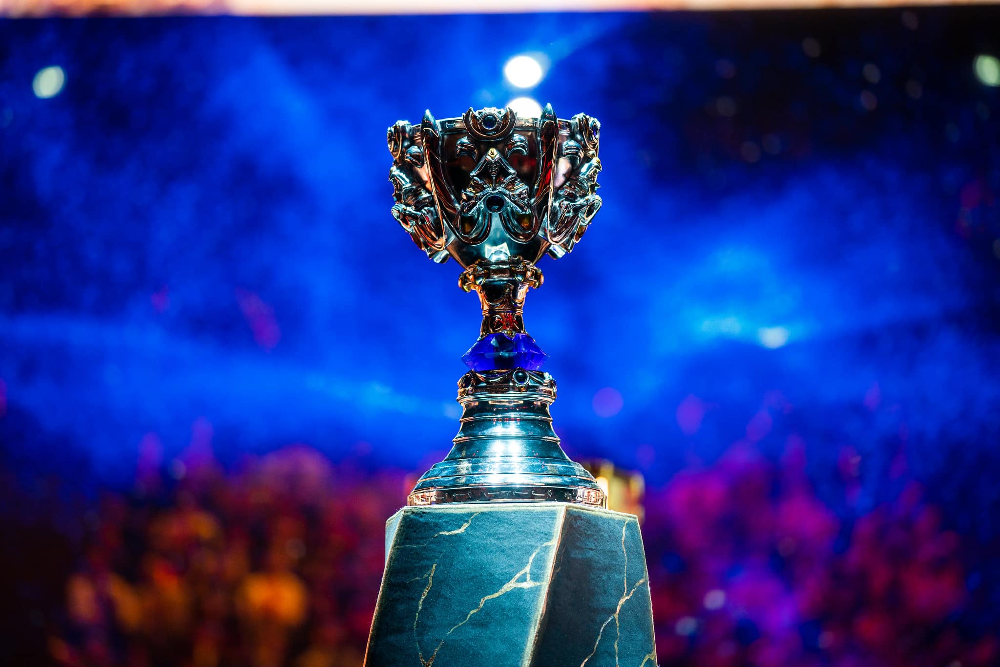 A silver trophy with intricate designs rests on a marble pedestal. The background features a vibrant, colorful light display with hues of blue and purple, giving the scene an energetic and celebratory atmosphere, reminiscent of the excellence achieved through OnlyBoosters.gg's LoL Boosting Services.