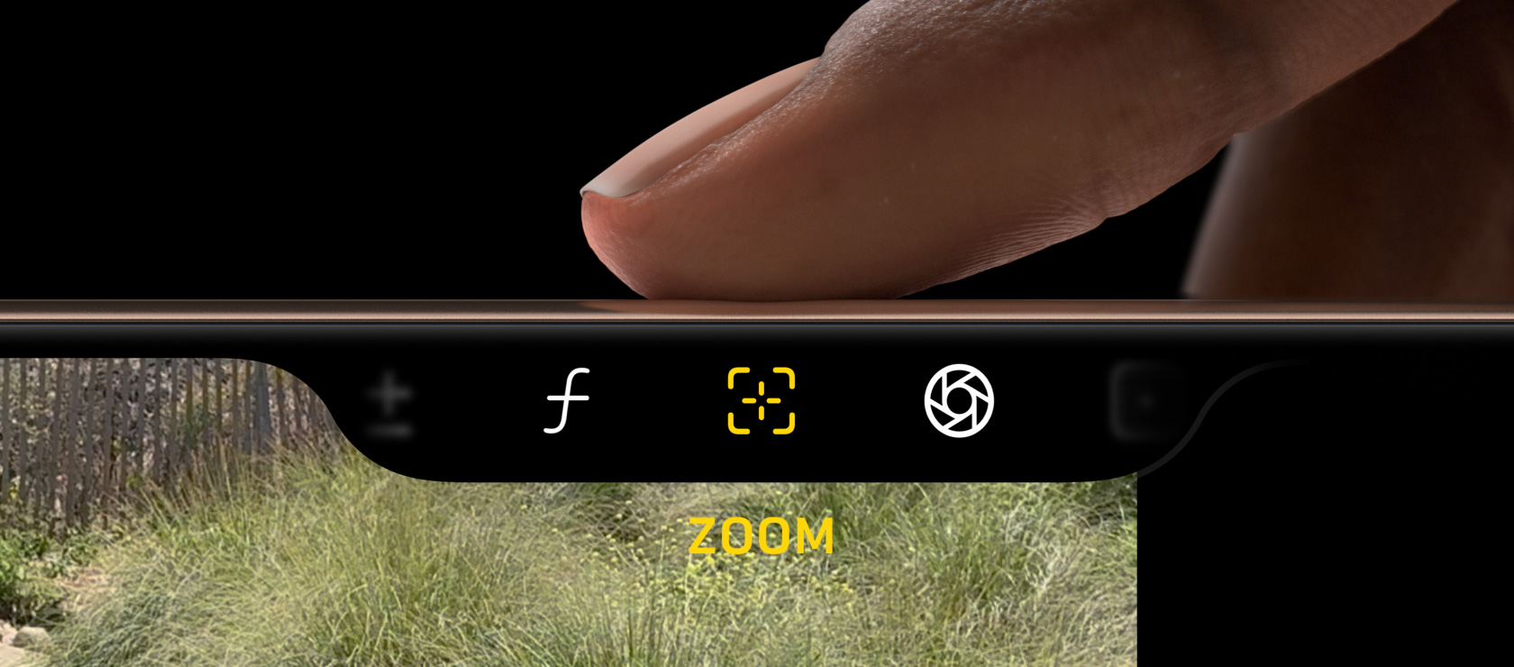 A close-up of a person's fingers adjusting the camera settings on a new iPhone 16. The interface shows icons for aperture, focus, and lens selection, with the word "ZOOM" visible on the screen display below.