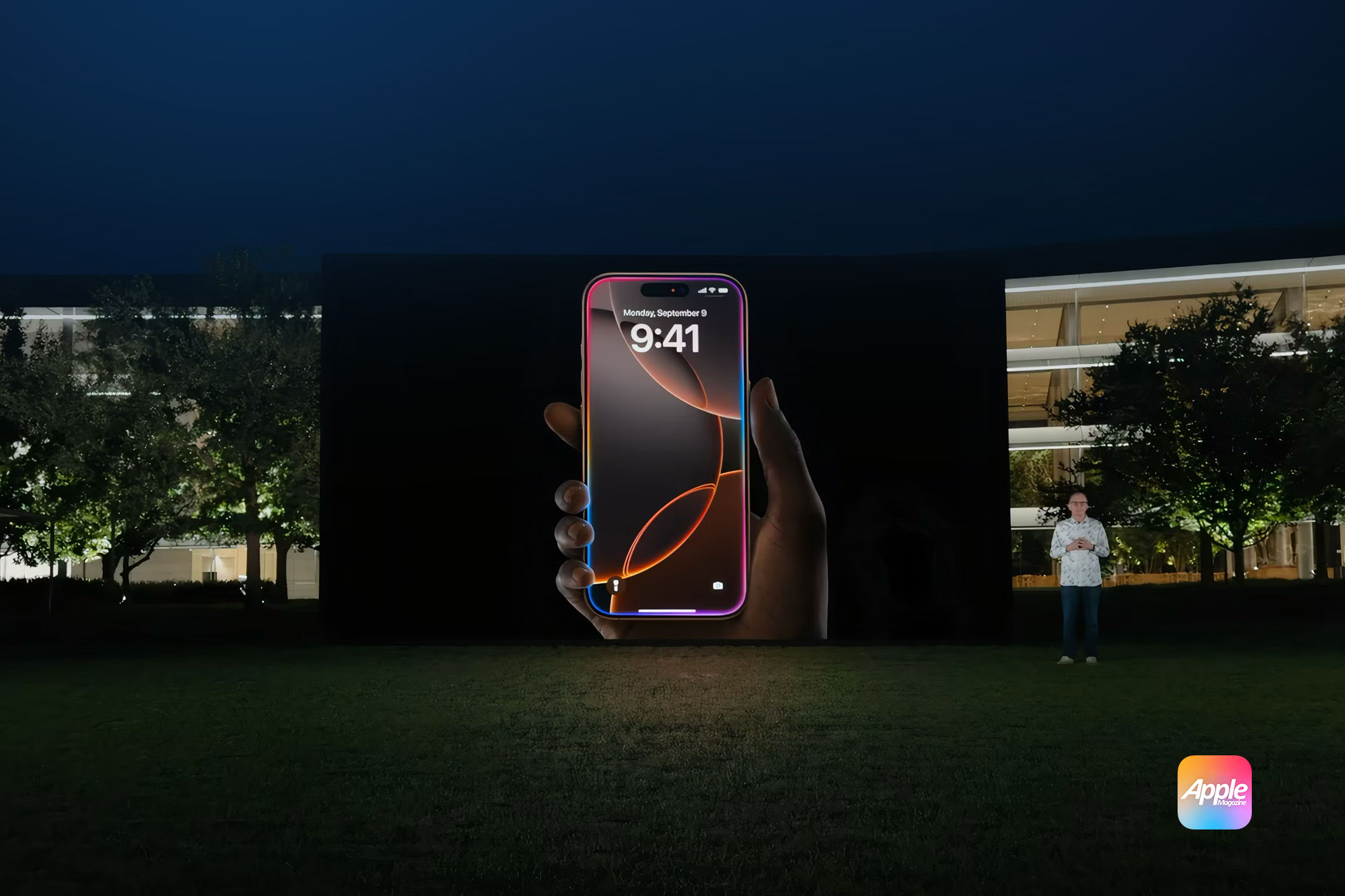 A large projection screen displays an enlarged image of a smartphone showing the time "9:41" and the date "Monday, September 12." A person stands to the right of the screen in front of a building. The Apple logo is visible in the bottom right corner, with the new iPhone 16 prominently featured. | Apple Intelligence-powered smart display integrating with HomeKit and Siri.