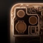 A close-up, top-down view of the internal circuitry and components of an electronic device, likely a smartphone, illuminated with a golden glow. The Apple logo is visible in the bottom-right corner. The background is black, highlighting the intricate details.