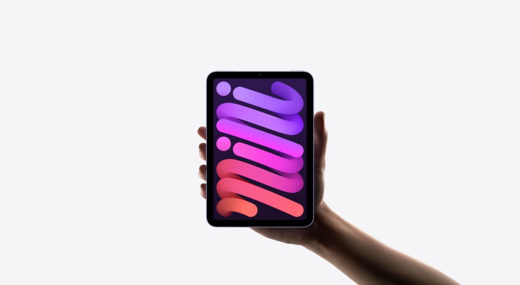 A hand holding an iPad Mini 7 against a white background. The iPad Mini 7 screen displays a colorful gradient design with the word "mini" in bold, stylized letters.