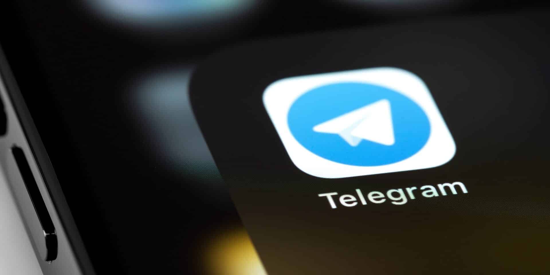 Close-up view of a smartphone screen with the Telegram message app icon prominently displayed in the foreground. The icon features a white paper plane on a blue circular background, with the word "Telegram" written below it.