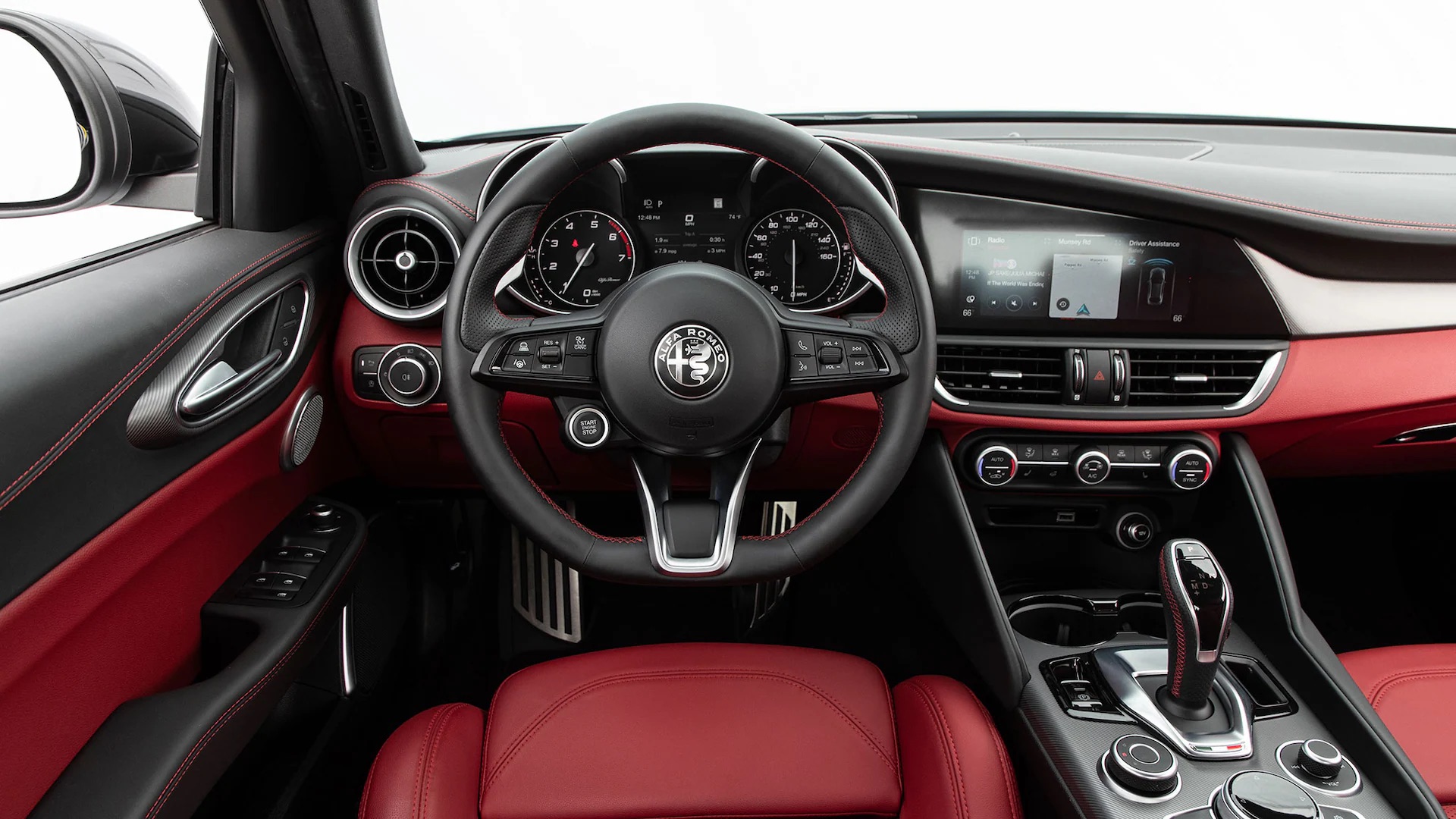 Interior view of an Alfa Romeo featuring a stylish black and red dashboard. The steering wheel displays the car brand's logo, and the console includes various controls, a touchscreen infotainment system, and a gear shifter. The seats are upholstered in red leather, complementing its luxurious feel.