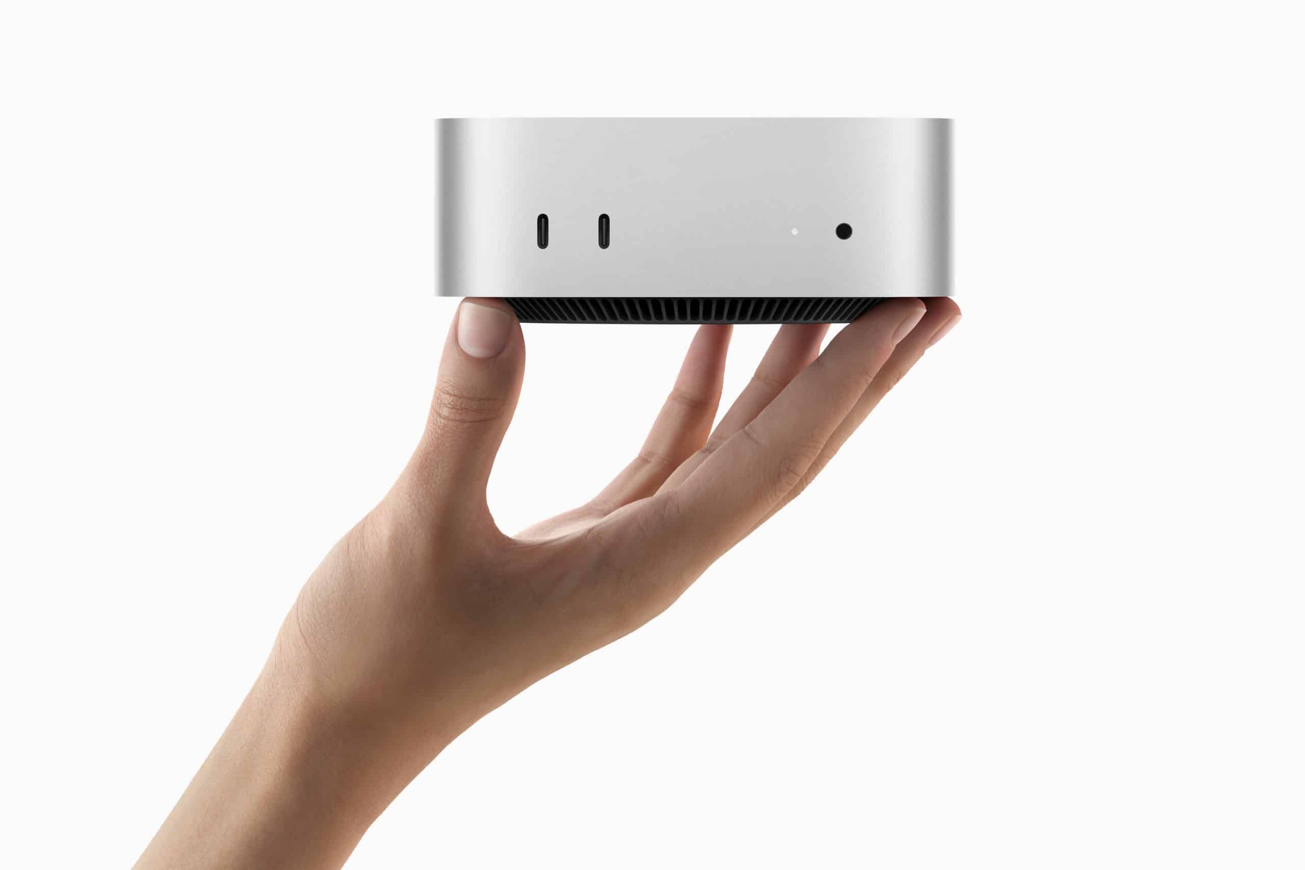 A hand holds a compact, silver electronic device with a minimalist design, echoing the sleekness of an Apple product. Its front features multiple small ports, reminiscent of the efficient layout found in devices like the Mac mini. The plain white background highlights its elegance.