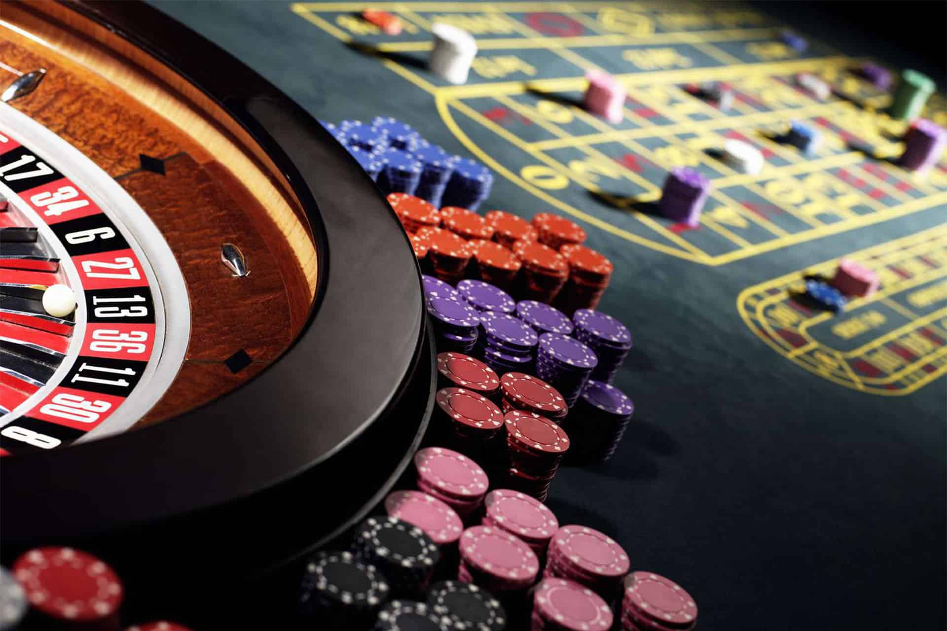 A roulette wheel with a ball resting on a number is on the left. Stacks of colorful poker chips are arranged on the table, hinting at the thrill of Casinos. Part of the betting layout is visible on the right.