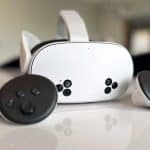 A Meta Quest 3S virtual reality headset with two matching controllers placed on a smooth, reflective surface. The headset features a sleek design with several buttons, and the controllers are positioned on either side. The background is softly blurred.