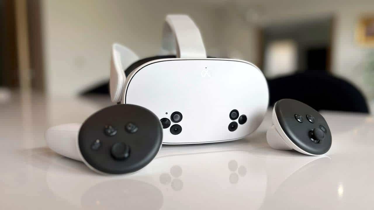 A Meta Quest 3S virtual reality headset with two matching controllers placed on a smooth, reflective surface. The headset features a sleek design with several buttons, and the controllers are positioned on either side. The background is softly blurred.