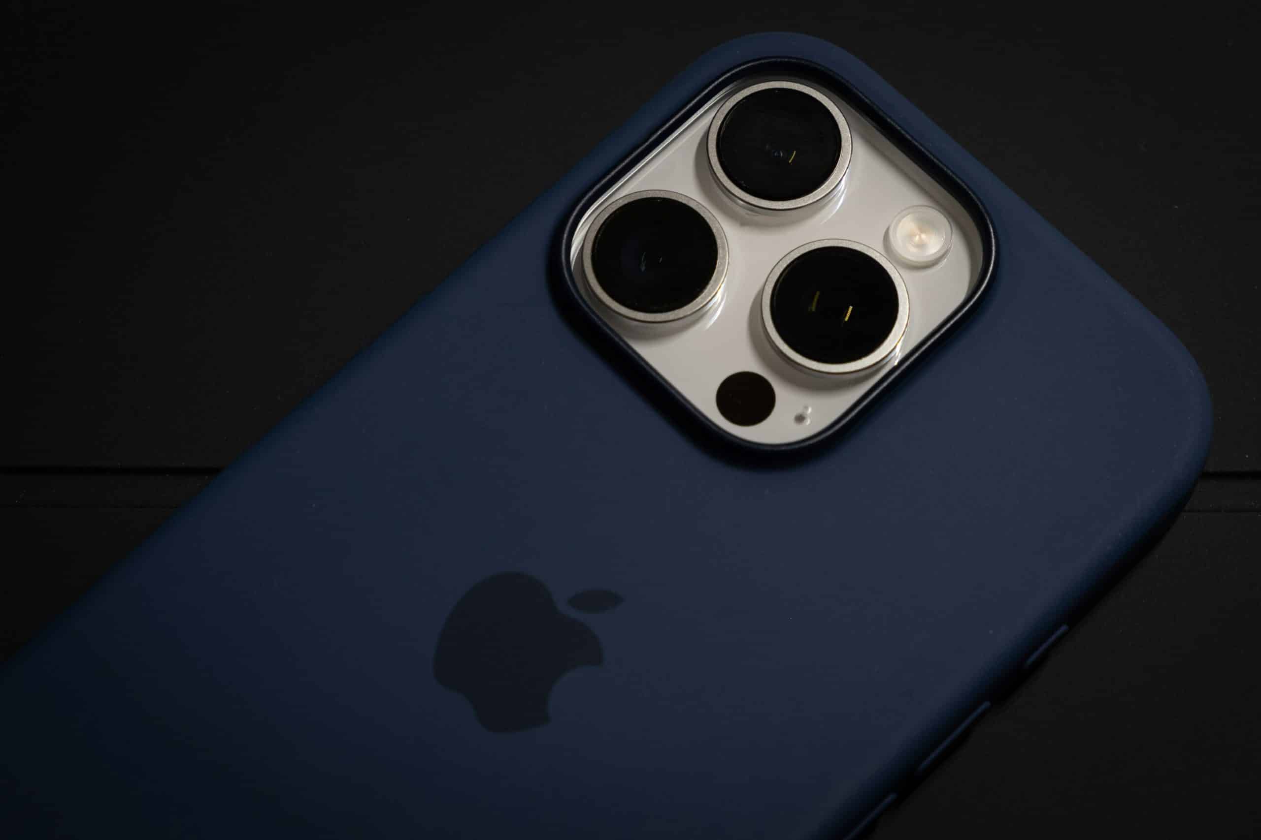 Close-up view of a smartphone with three camera lenses and a dark blue case, placed on a black surface.