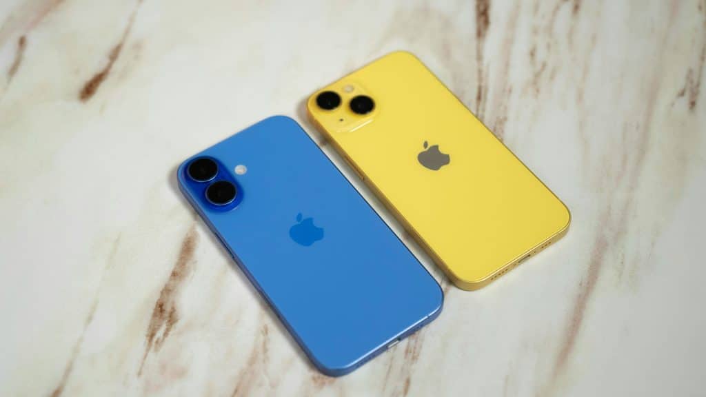 Two iPhones are placed on a marble surface. One is blue and the other is yellow, both featuring the Apple logo on the back. The phones are positioned side by side, showcasing their dual-camera setups.