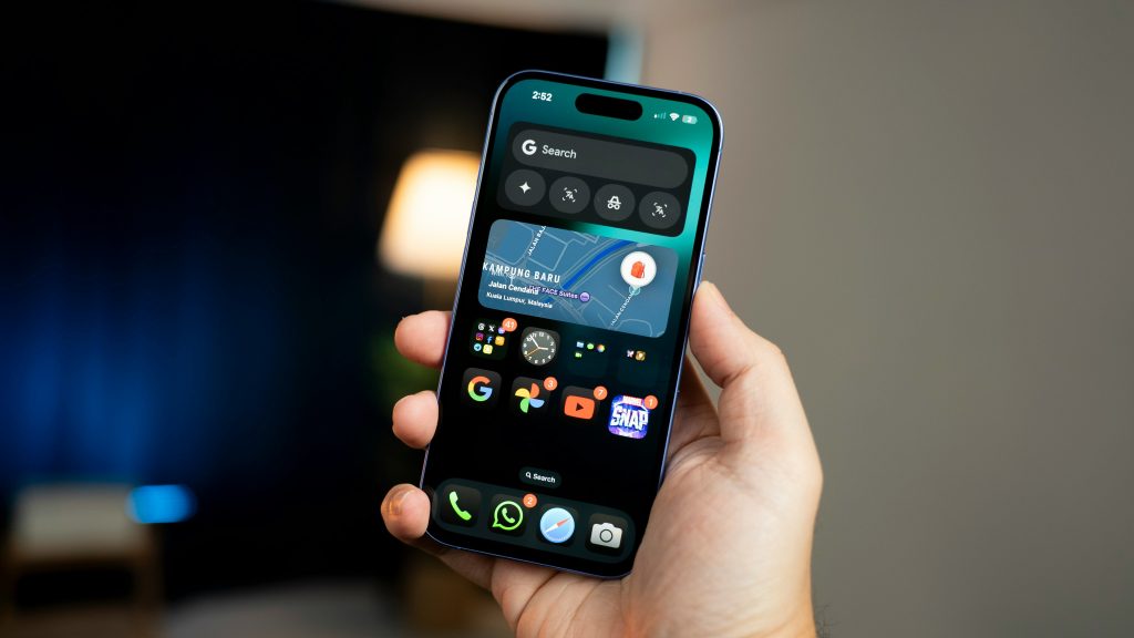 A hand holds a smartphone displaying a home screen with various app icons and widgets. The screen shows a map, weather details, and applications like Google, YouTube, and Instagram. The phone is set against a blurred background.