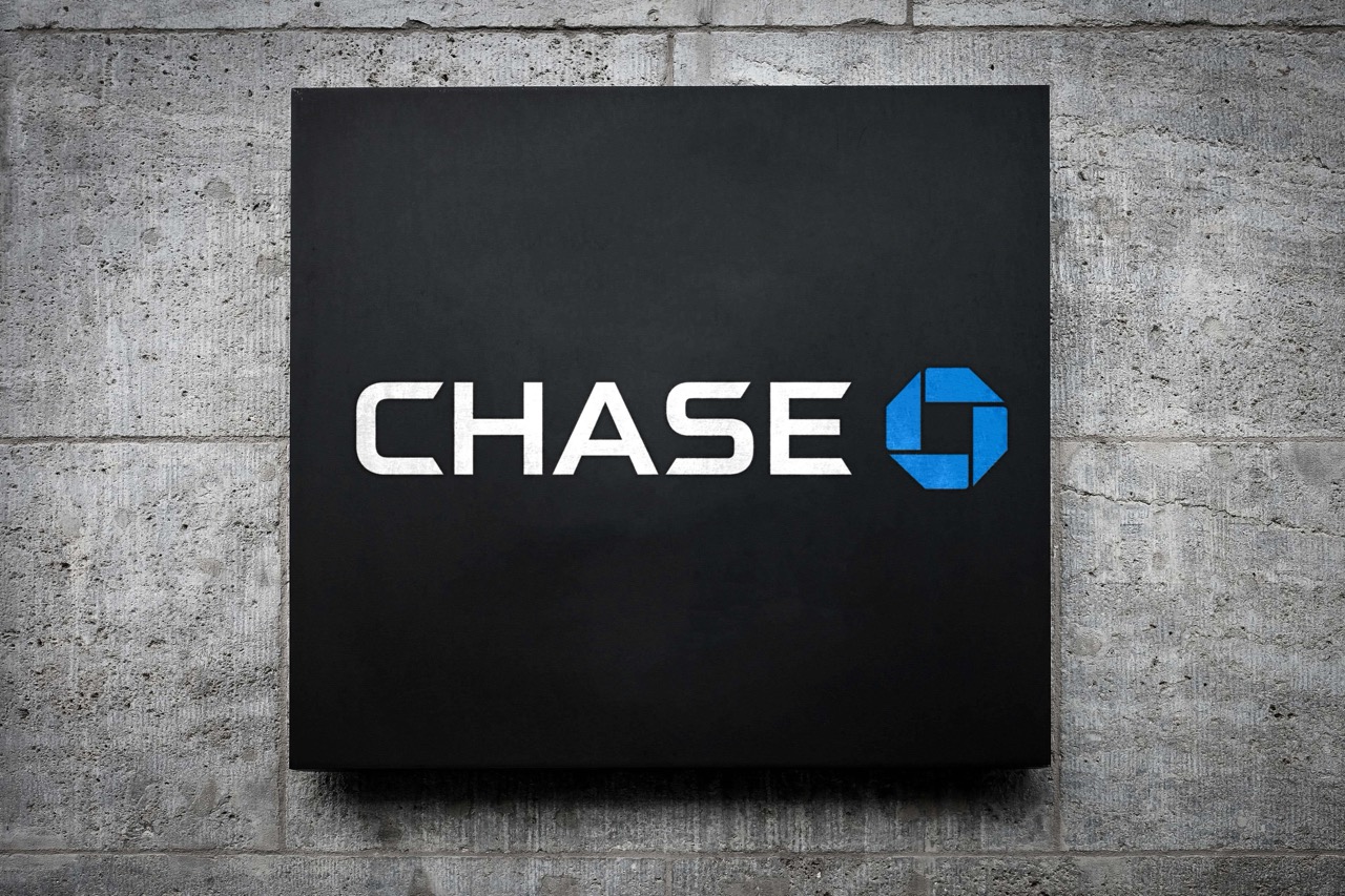 A black square sign with the word "CHASE" in white capital letters is displayed next to a blue octagonal logo, representing Chase Bank. The sign is mounted on a textured gray stone wall, making it a distinctive presence among banks for business.