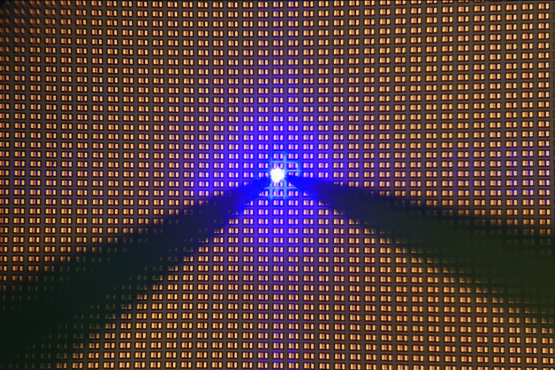 A grid of orange squares with a bright blue light at the center, reminiscent of cutting-edge MicroLED displays, surrounded by two beams of blue light extending outward, creating a vibrant, geometric pattern.