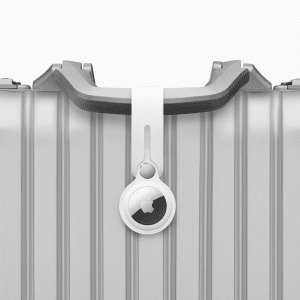 A silver suitcase with a ridged design features an Apple AirTag securely attached to its handle using a white loop. The suitcase proudly displays the Apple logo, hinting at a collaboration with Apple’s innovative AirTags technology.