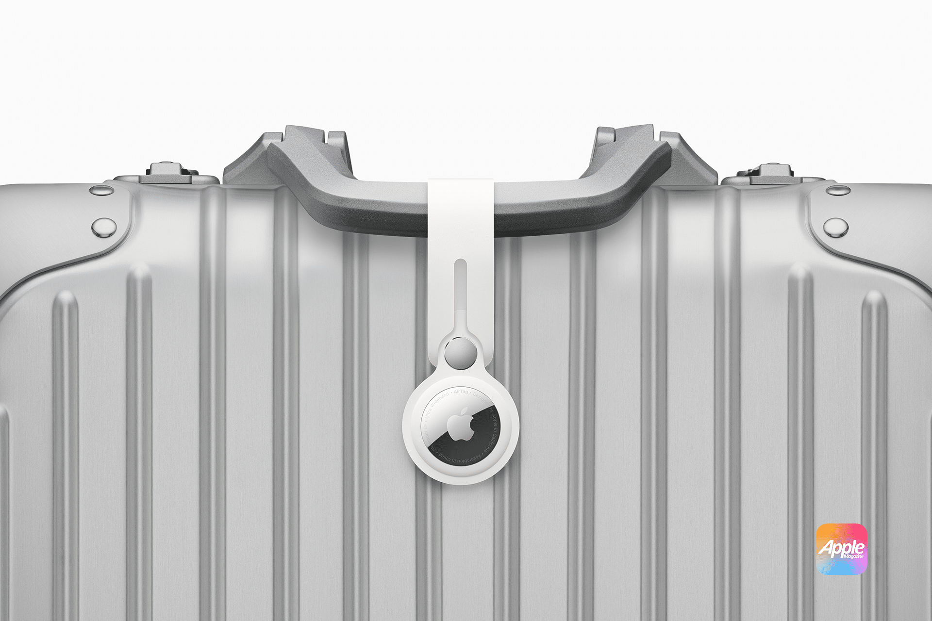 A silver suitcase with a ridged design features an Apple AirTag securely attached to its handle using a white loop. The suitcase proudly displays the Apple logo, hinting at a collaboration with Apple’s innovative AirTags technology.