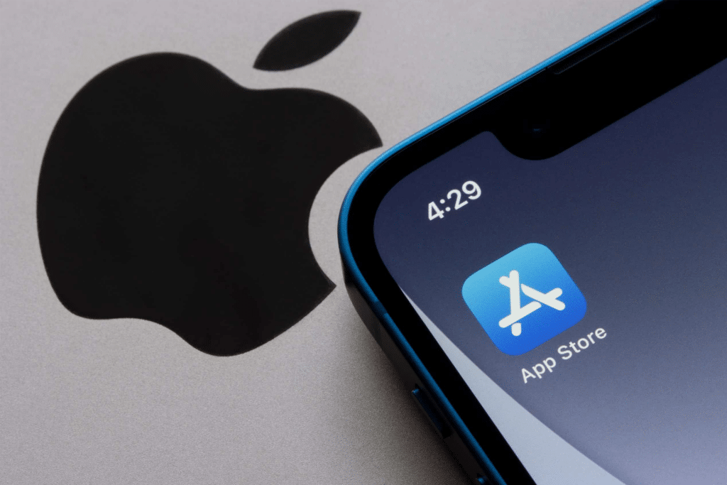 A close-up of an iPhone screen reveals recent App Store changes, with the familiar icon set against a blue background and a stylized white "A." The phone's time reads 4:29, while the iconic Apple logo subtly enhances the backdrop.