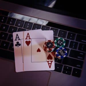 Two Aces of Clubs and Hearts on a laptop keyboard surrounded by poker chips in various denominations and colors, including green 25, purple 500, and red 5.