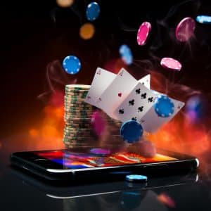 A smartphone displays a poker game, surrounded by flying poker chips and playing cards, including four aces. Stacks of chips stand on the phone, against a fiery, blurred background.