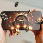 Hands holding a smartphone displaying a virtual casino scene with poker chips, dice, playing cards, and a roulette wheel appearing to pop out from the screen in a 3D effect.
