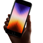 A hand holds an iPhone SE 4th Gen, showcasing a gradient wallpaper with vertical stripes in shades of purple, pink, and orange. The phone features a black front with a circular home button, and the iconic Apple logo is visible in the bottom right corner.