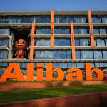 A large orange "Alibaba" sign stands proudly in front of a modern glass building with vertical orange accents, reflecting the vibrant tech spirit of China. A brown character statue graces the balcony, while the sun shines brightly, casting clear shadows reminiscent of Apple's design intelligence.