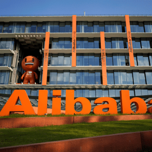 A large orange "Alibaba" sign stands proudly in front of a modern glass building with vertical orange accents, reflecting the vibrant tech spirit of China. A brown character statue graces the balcony, while the sun shines brightly, casting clear shadows reminiscent of Apple's design intelligence.