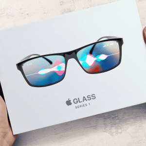 A pair of standalone AR glasses with a digital interface on the lenses, displaying colorful graphics and icons, are placed on top of a white Apple Glass Series 1 box. The box is cradled by two hands on a light wooden surface.