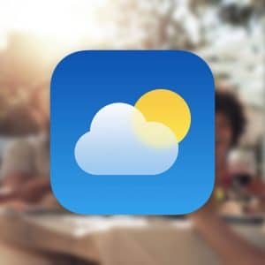 A weather app icon featuring a cloud and sun is centered over a blurred background of people enjoying an outdoor meal, seamlessly integrating into the Apple ecosystem. The Apple logo adorns the bottom right corner.