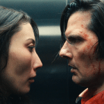 A woman and a man with blood on his face stand very close, staring intensely at each other in a dimly lit setting, evoking the tense atmosphere of Severance.