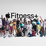 A diverse group of people in athletic wear pose happily together in The Studio, in front of a white background with a large “Apple Fitness+” logo displayed above them.