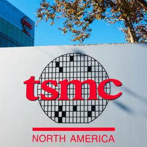 A sign featuring the TSMC logo and the words "North America" in red stands prominently, with a modern building and trees in the background beneath a clear blue sky.