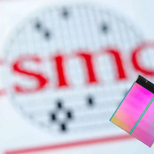 A pair of tweezers holds a colorful silicon chip in the foreground, with the blurred TSMC logo in red and black visible in the background.