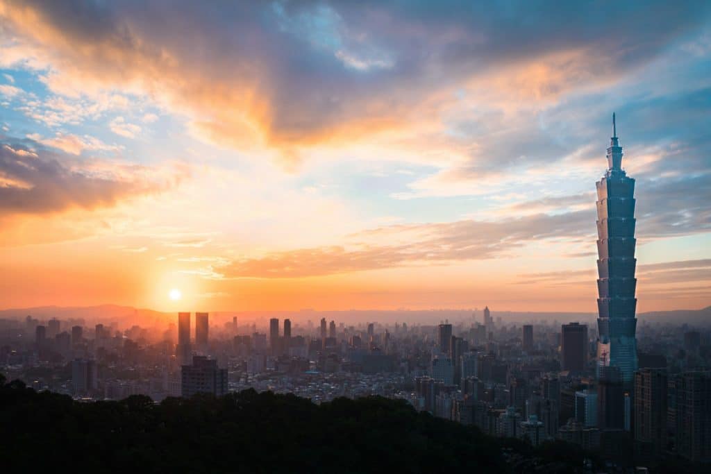 Taipei city skyline at sunset, with Taipei 101 tower prominently rising on the right—an iconic sight in Taiwan perfect for sightseeing beneath a colorful sky as the sun sets behind scattered clouds.