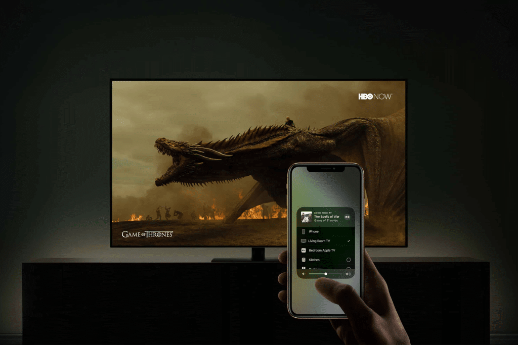A hand holds a smartphone in front of a TV displaying a Game of Thrones dragon scene. The phone shows an AirPlay media control screen, seamlessly streaming content to the TV.