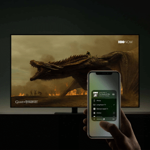 A hand holds a smartphone in front of a TV displaying a Game of Thrones dragon scene. The phone shows an AirPlay media control screen, seamlessly streaming content to the TV.
